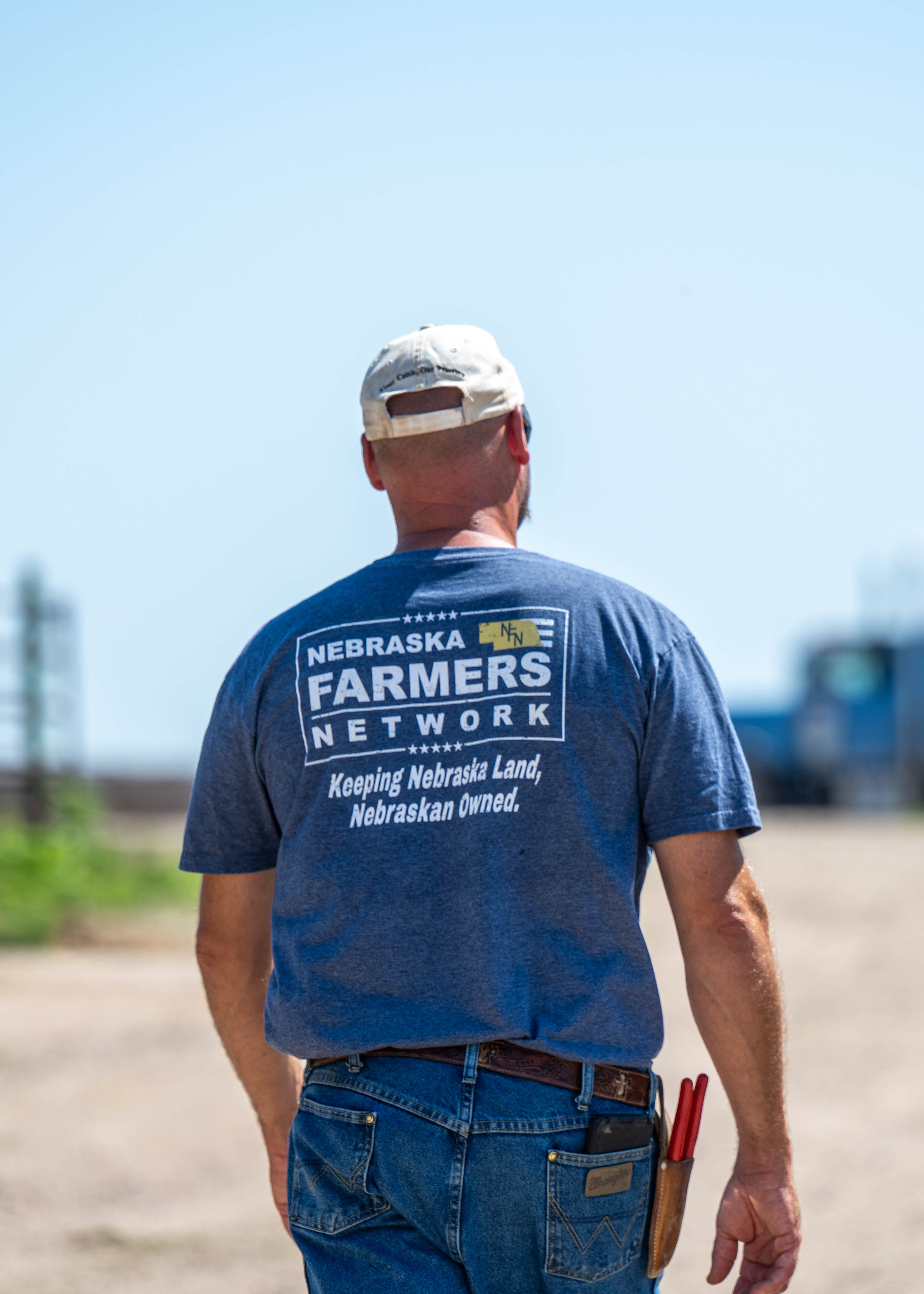 A Nebraska Farmers Network member walking a dirt farm road wearing an NFN branded shirt — Keeping Nebraska Land, Nebraskan Owned.